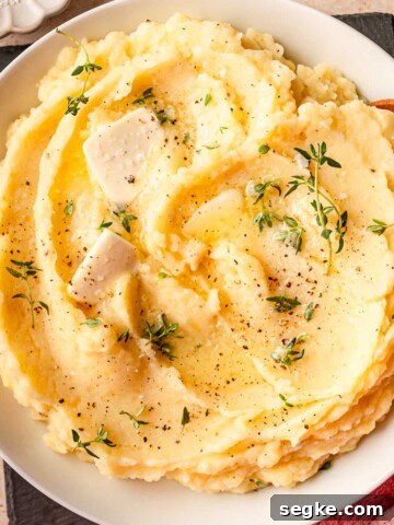 Mashed potatoes topped with butter slices and fresh thyme.