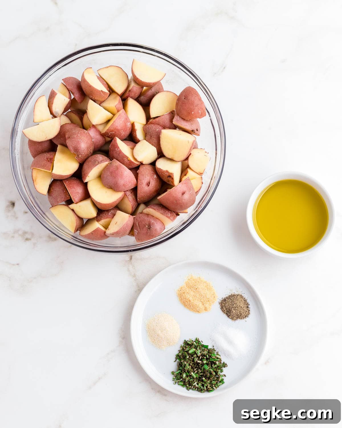Perfectly Crispy Air Fryer Red Potatoes 2 Red potatoes cut into small pieces in a glass bowl with oil and spices on the side.