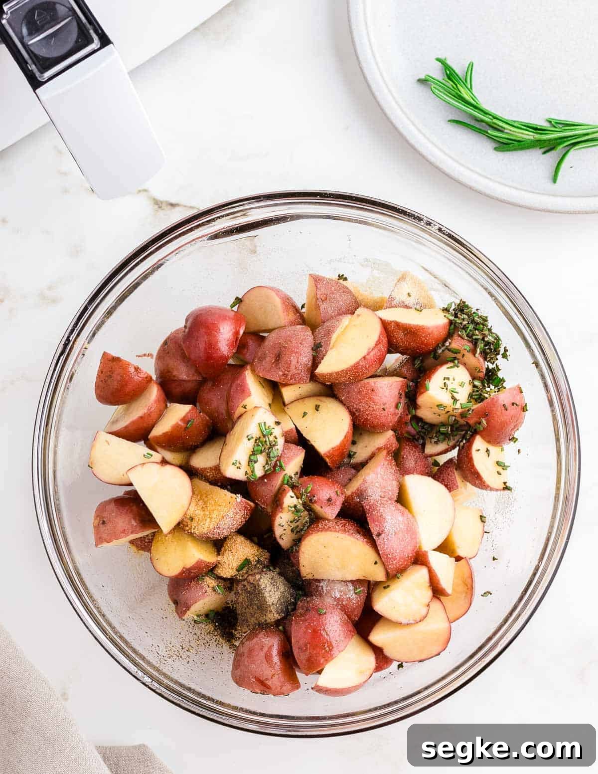 Perfectly Crispy Air Fryer Red Potatoes 3 Red potatoes cut into chunks with fresh minced rosemary and spices in a glass bowl.