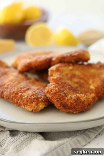 crispy chicken fritter on a plate with lemons and parmesan cheese in the background