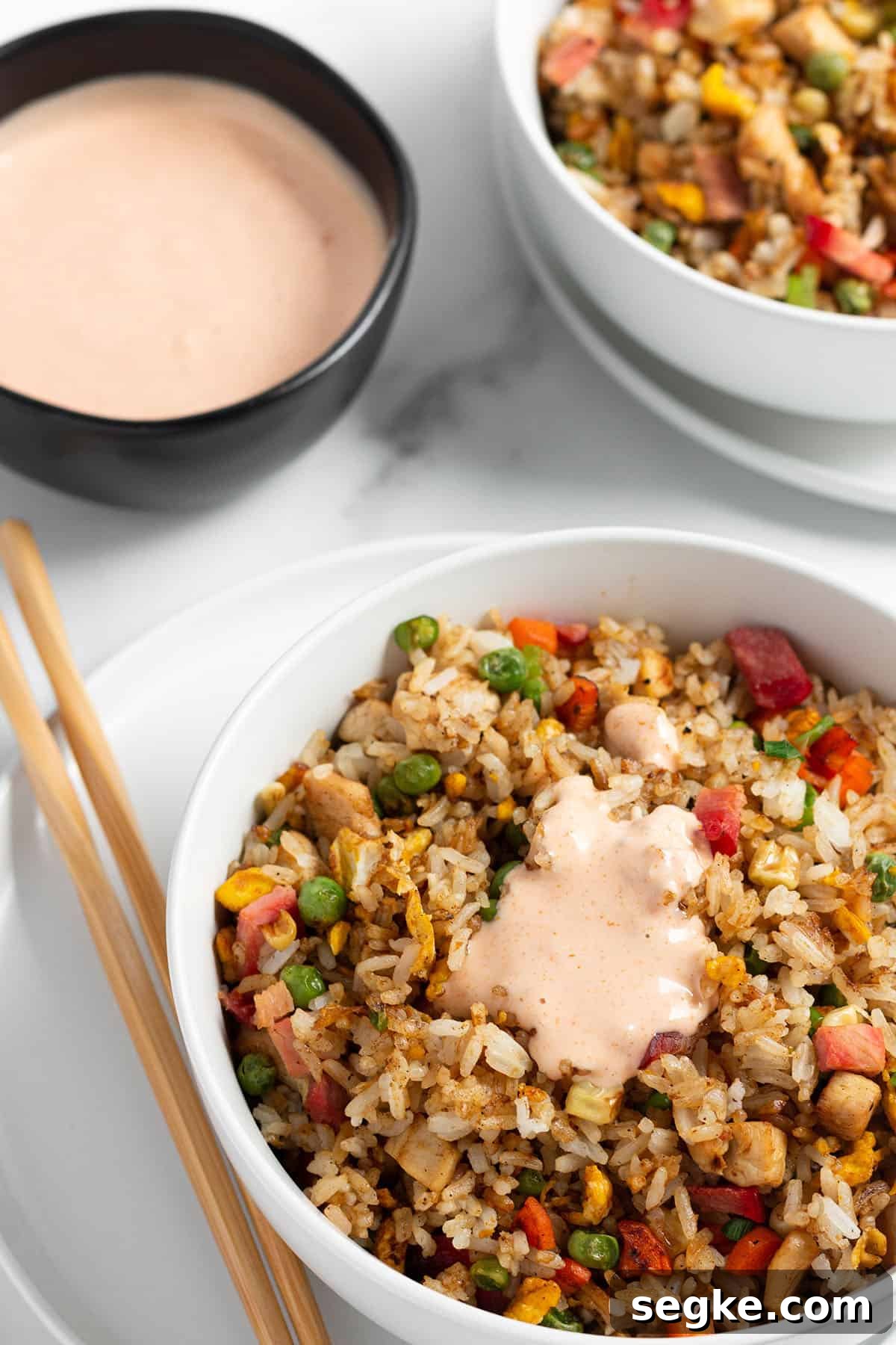 Two bowls with fried rice with a bowl of yum yum sauce. 