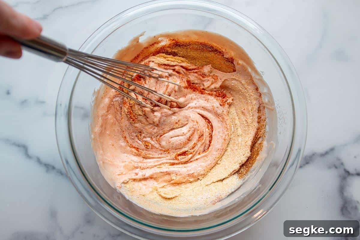 Glass bowl with whisk mixing spices in mayo and ketchup mix.