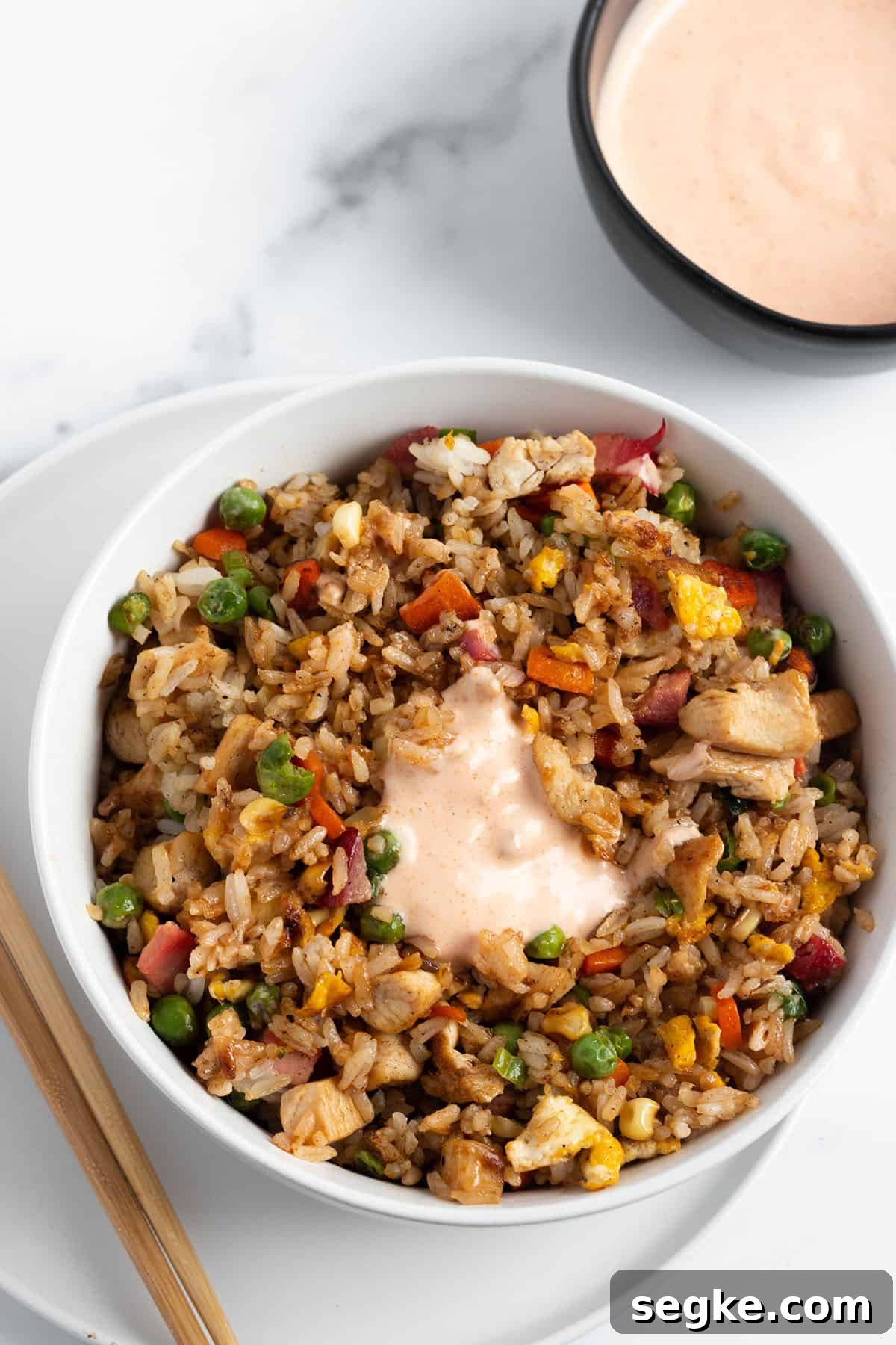 A bowl of fried rice with yum yum sauce on top and in a bowl.