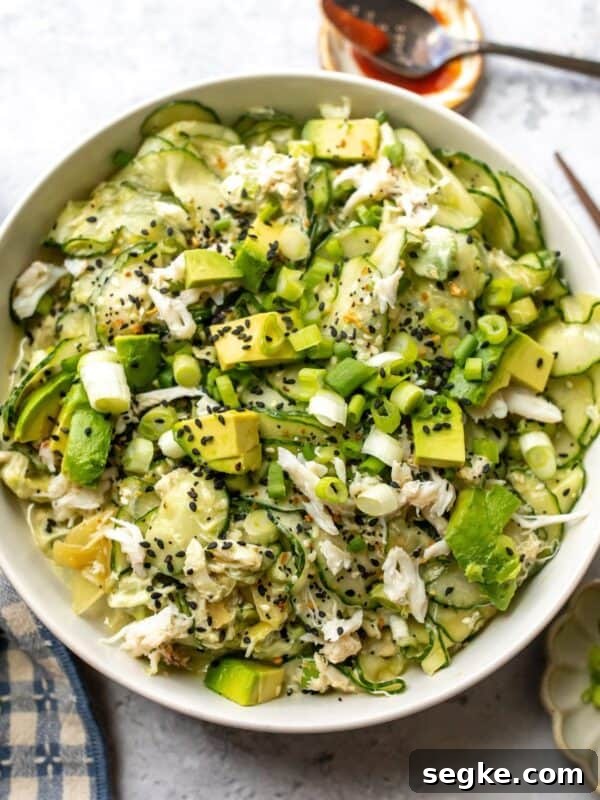 White bowl with California Roll Cucumber Salad topped with avocado and sesame seeds.
