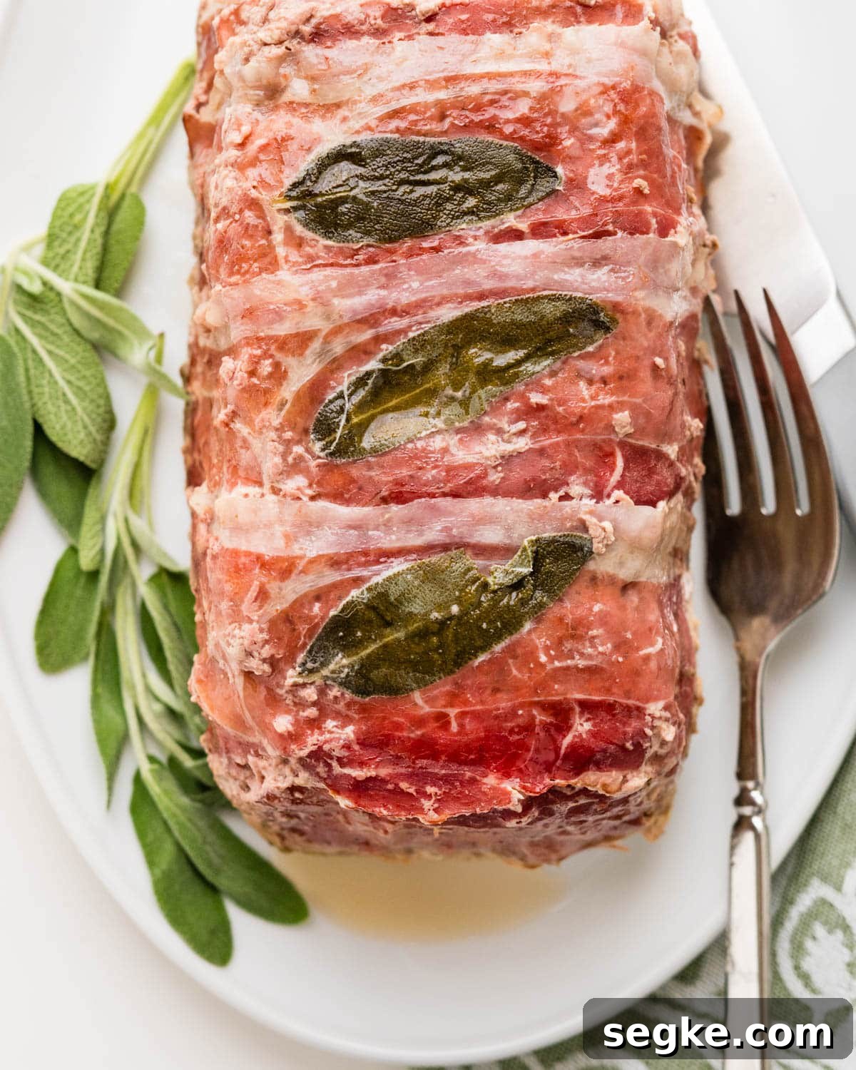 Oven Baked Meatloaf with Creamy Mushroom Gravy 5 wrapped veal, beef and pork meatloaf with fresh sage leaves on a platter.