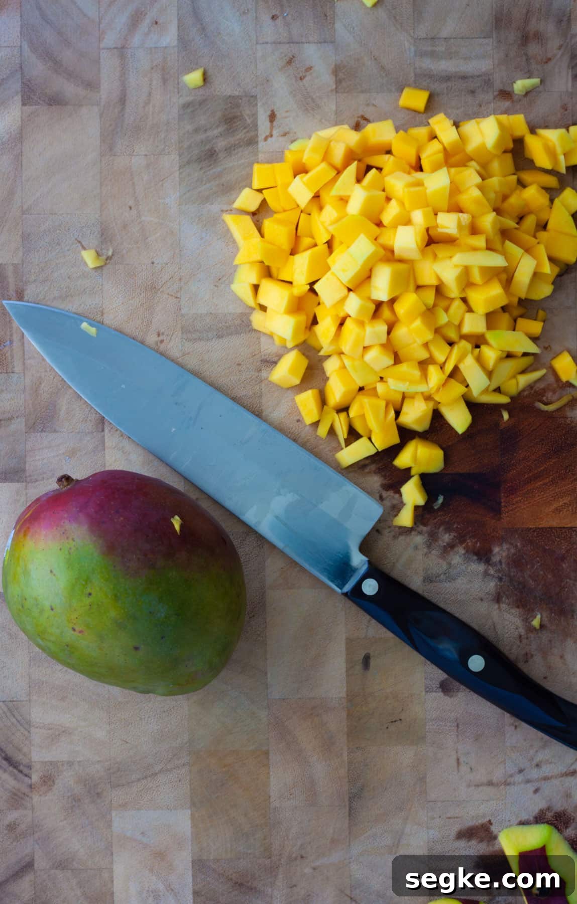 Chopped mango on a cutting board with a second unpeeled mango just to the side.