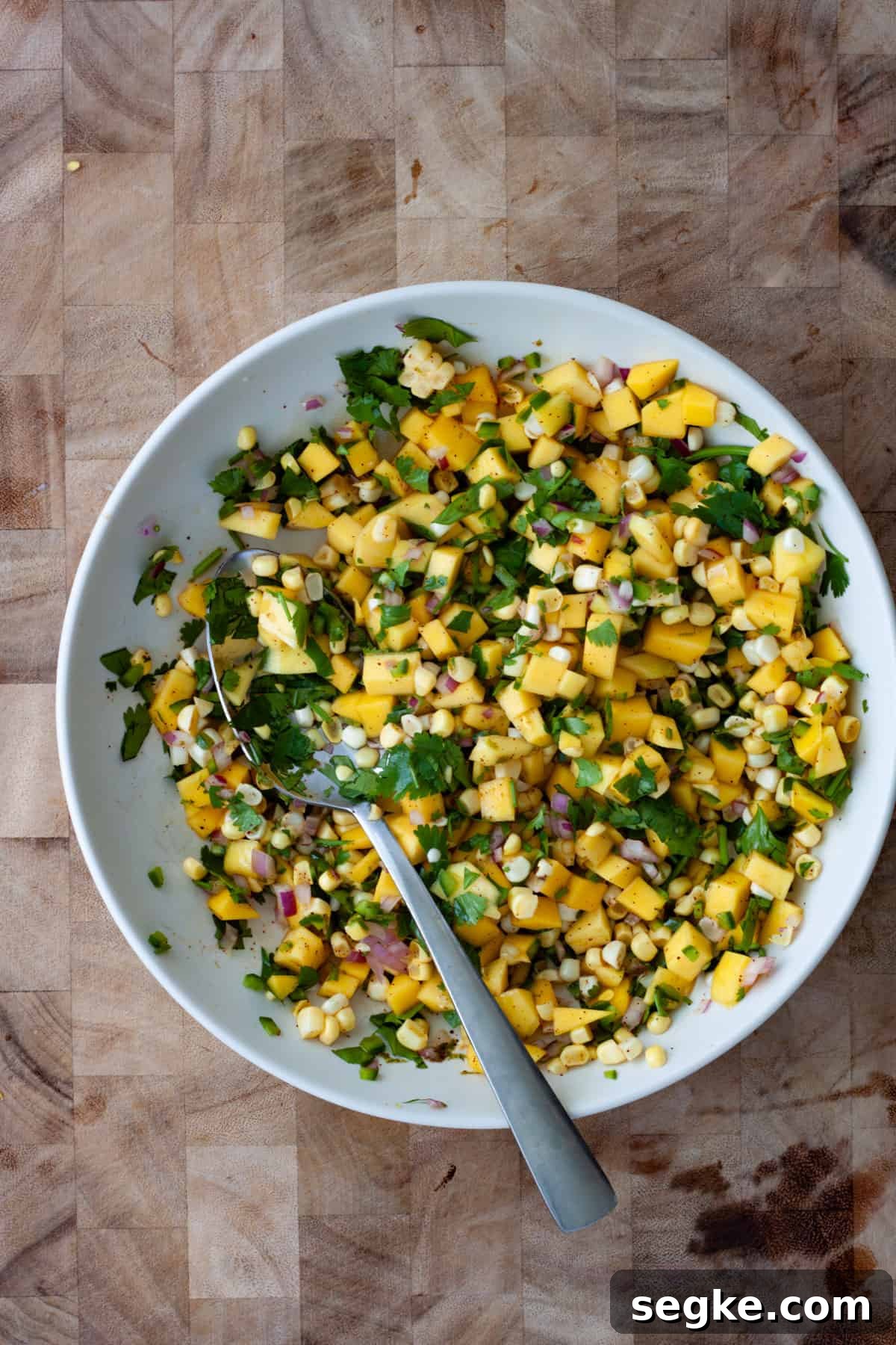 Mango and corn salsa in a medium mixing bowl with a spoon.