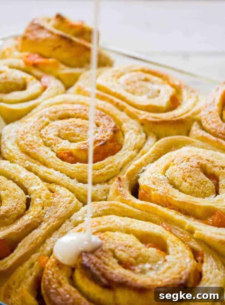 A glaze being drizzled over a pan of sweet rolls.