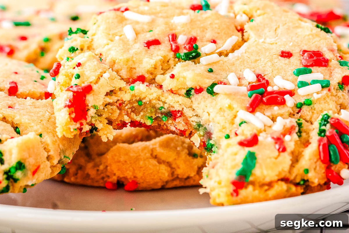 Close-up of a soft Christmas sprinkle sugar cookie with a bite taken out, showing chewy center and colorful sprinkles baked into the dough.