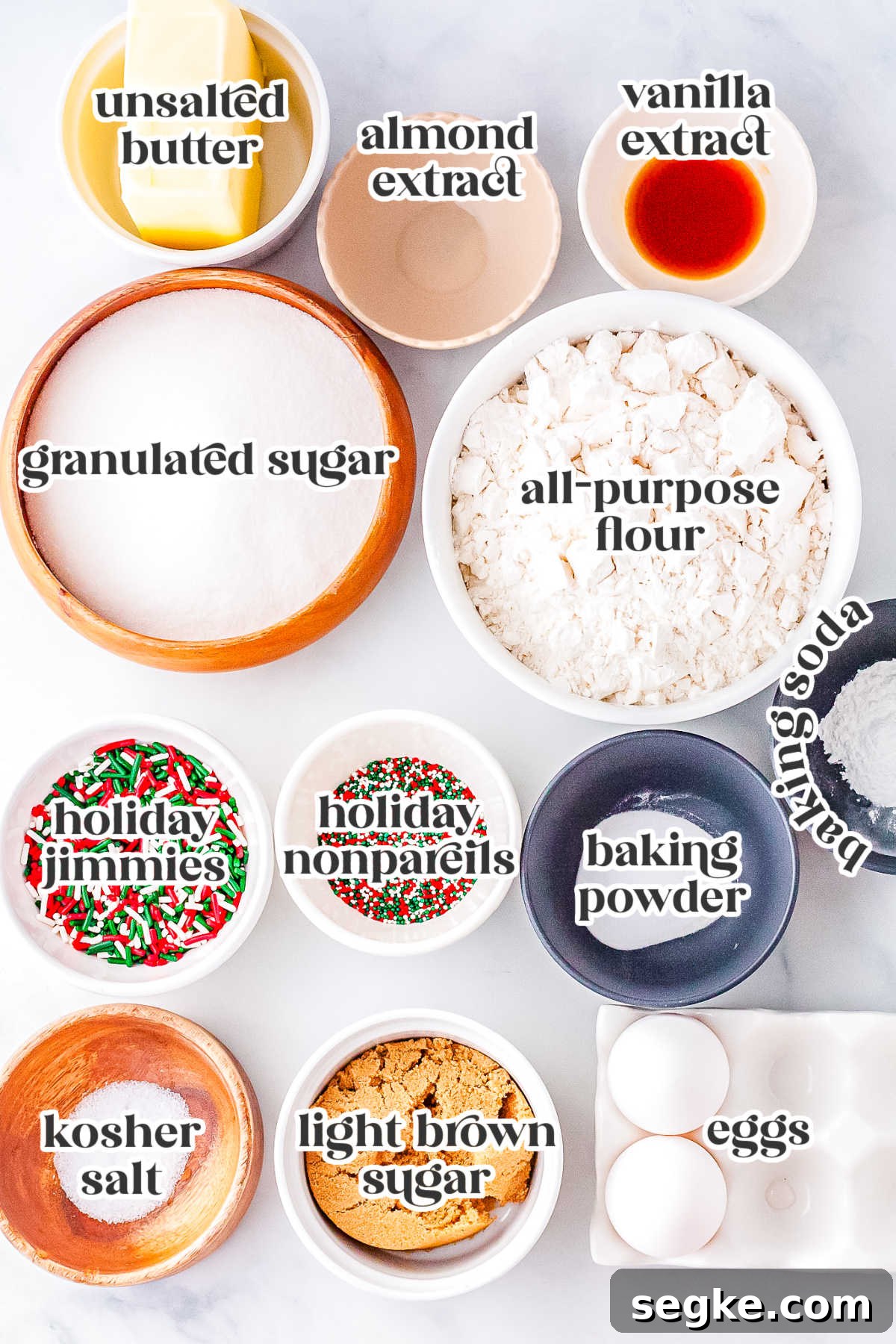 Measured ingredients for Christmas sprinkle sugar cookies including flour, sugars, butter, eggs, vanilla, almond extract, and colorful holiday sprinkles arranged in bowls.