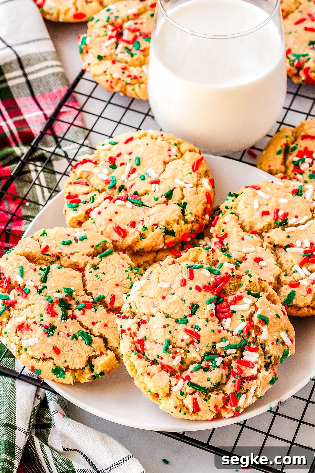 Plate of Christmas sprinkle sugar cookies next to a glass of milk on a cooling rack with festive red and green sprinkles, ready for holiday sharing.