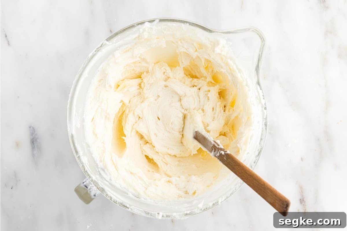 Funfetti Cake Recipe with Rainbow Sprinkles 12 Icing stirred with a spatula in a mixing bowl.