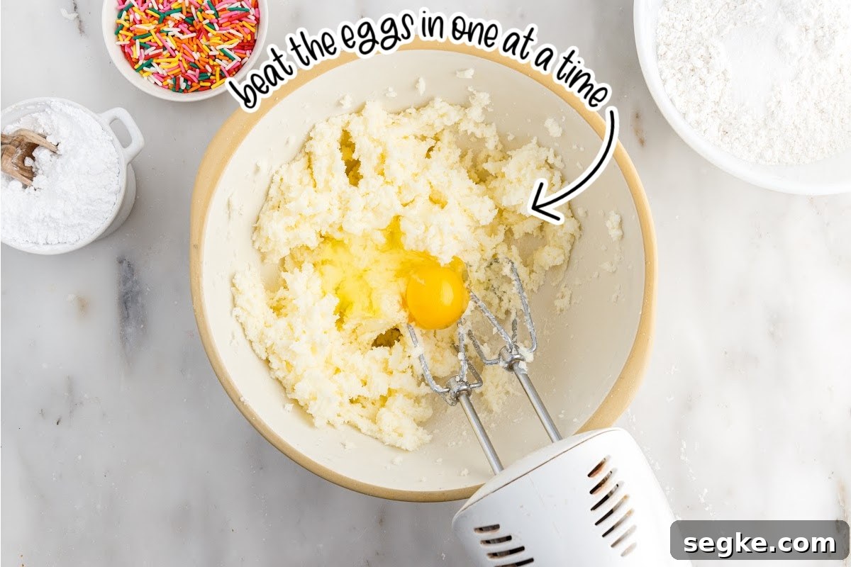 Funfetti Cake Recipe with Rainbow Sprinkles 4 Eggs added to sugar in a mixing bowl with a mixer with text overlay.