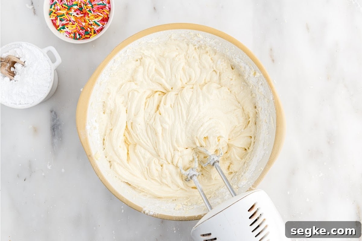 Funfetti Cake Recipe with Rainbow Sprinkles 7 Flour mixture added to wet mixture in a mixing bowl with a mixer inserted.