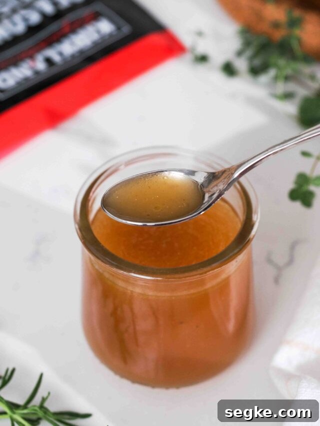 Instant Pot Chicken Bone Broth Recipe 13 A spoon with homemade chicken bone broth over a small glass jar.