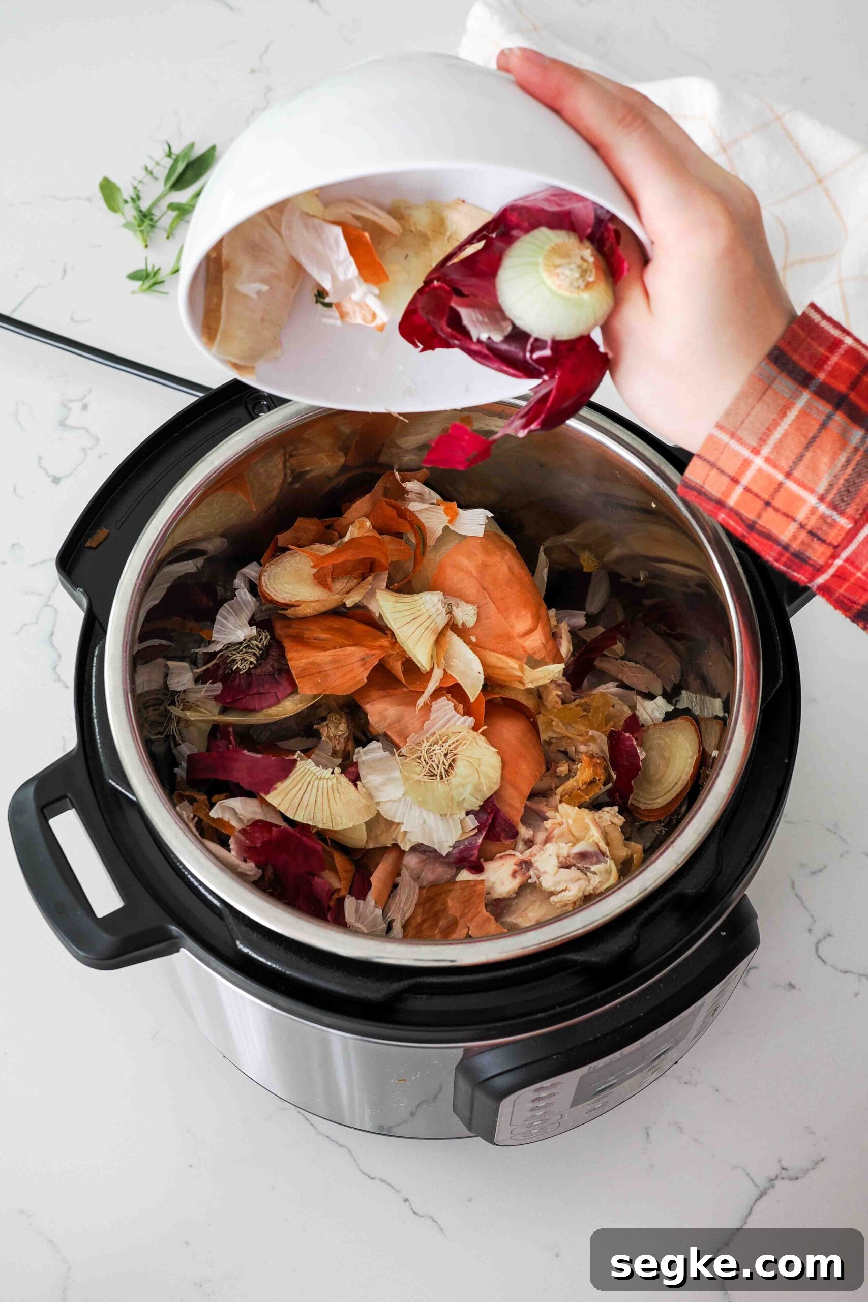 Instant Pot Chicken Bone Broth Recipe 5 A hand tips a bowl of vegetable scraps over the pot of an Instant Pot.