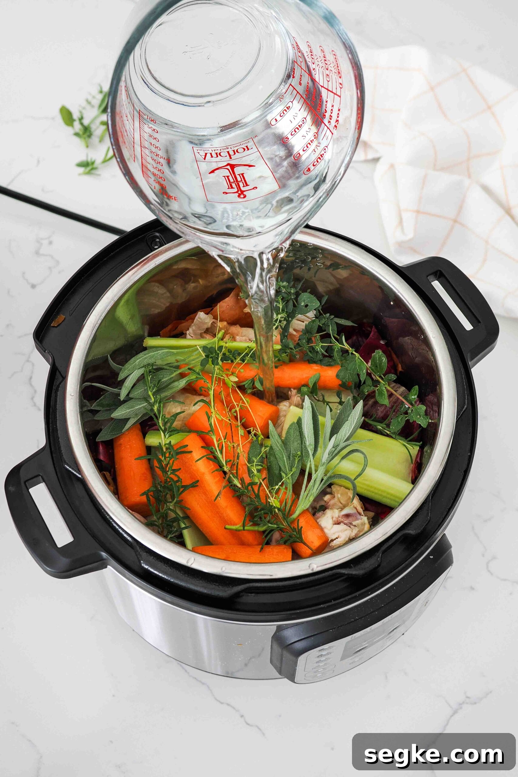 Instant Pot Chicken Bone Broth Recipe 7 Water is poured over vegetables, herbs, and chicken scraps in and Instant Pot.