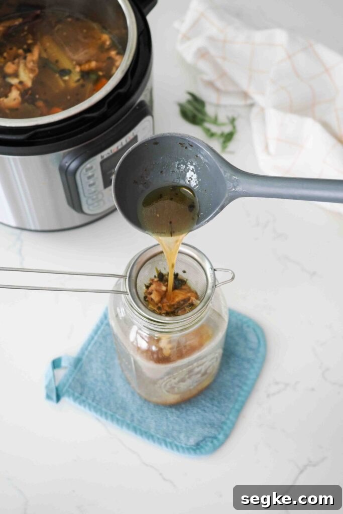 Instant Pot Chicken Bone Broth Recipe 10 A ladle pours chicken bone broth over a strainer and into a large glass jar.