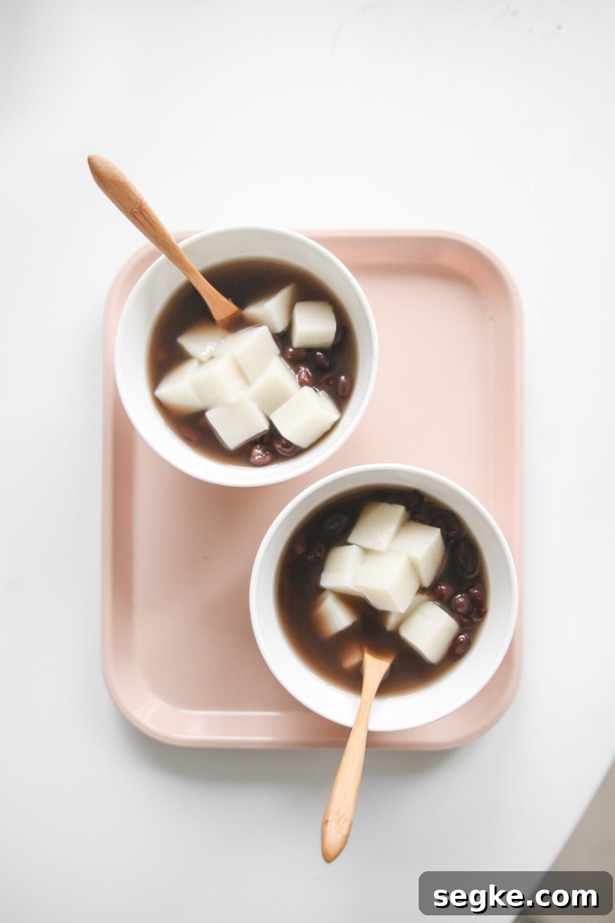 Japanese Zenzai Recipe: Sweet Red Bean Soup 4 two bowls of Japanese red bean soup topped with mochi with wooden spoons resting on the side.
