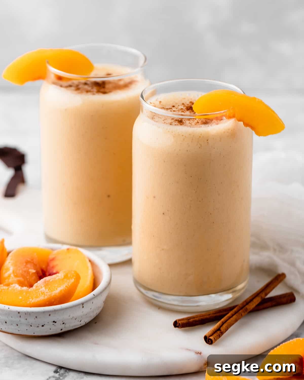 two glasses of Peach Smoothie garnished with peach slices and sprinkled with cinnamon