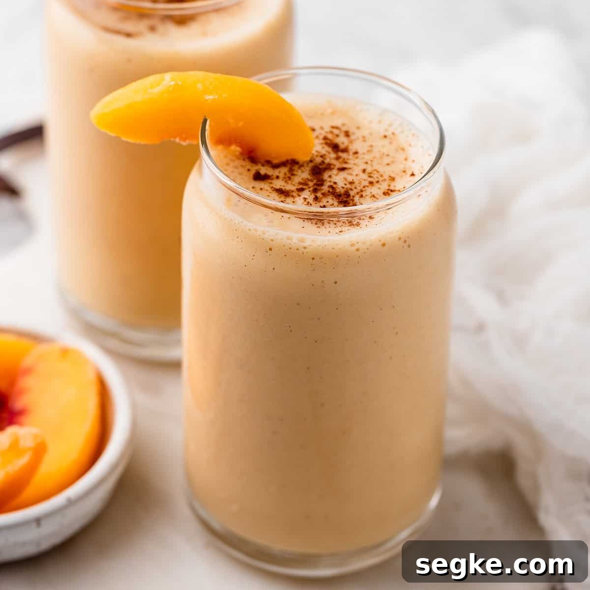 a glass of Peach Smoothie garnished with peach slices and sprinkled with cinnamon