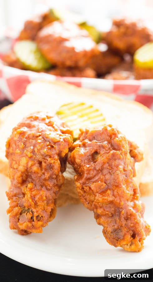 How to Make Crispy Nashville Hot Chicken Wings 5 Two Nashville Hot fried chicken wings next to a slice of white bread and a pickle slice.