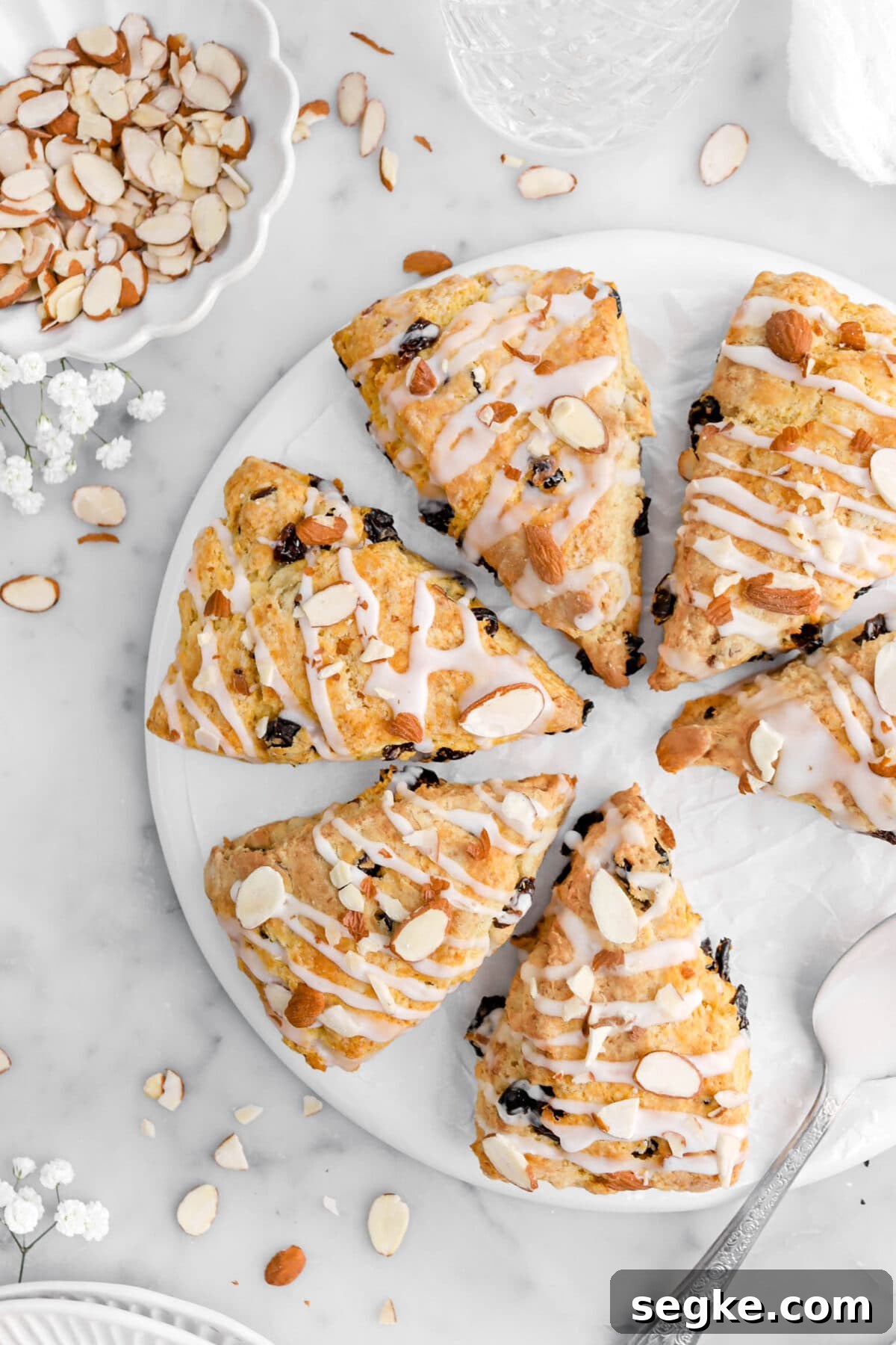 cropped close up of four scones on upside down plate with two more beside with almonds and flowers around.