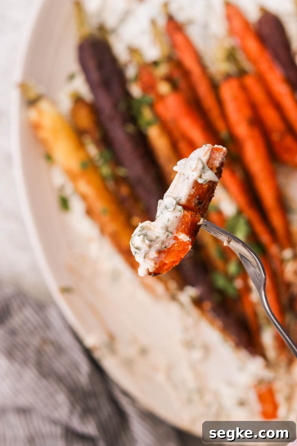 a fork holding a carrot dipped in yogurt sauce 