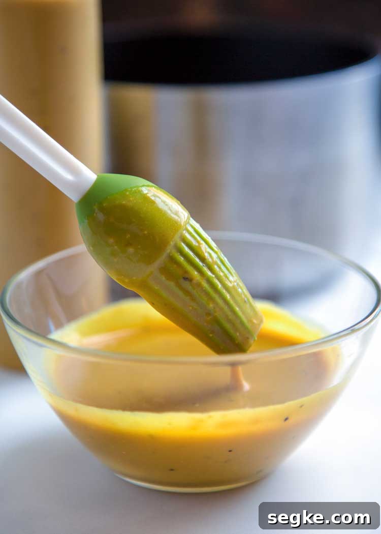 dipping green silicone basting brush into small glass bowl of mustard bbq sauce