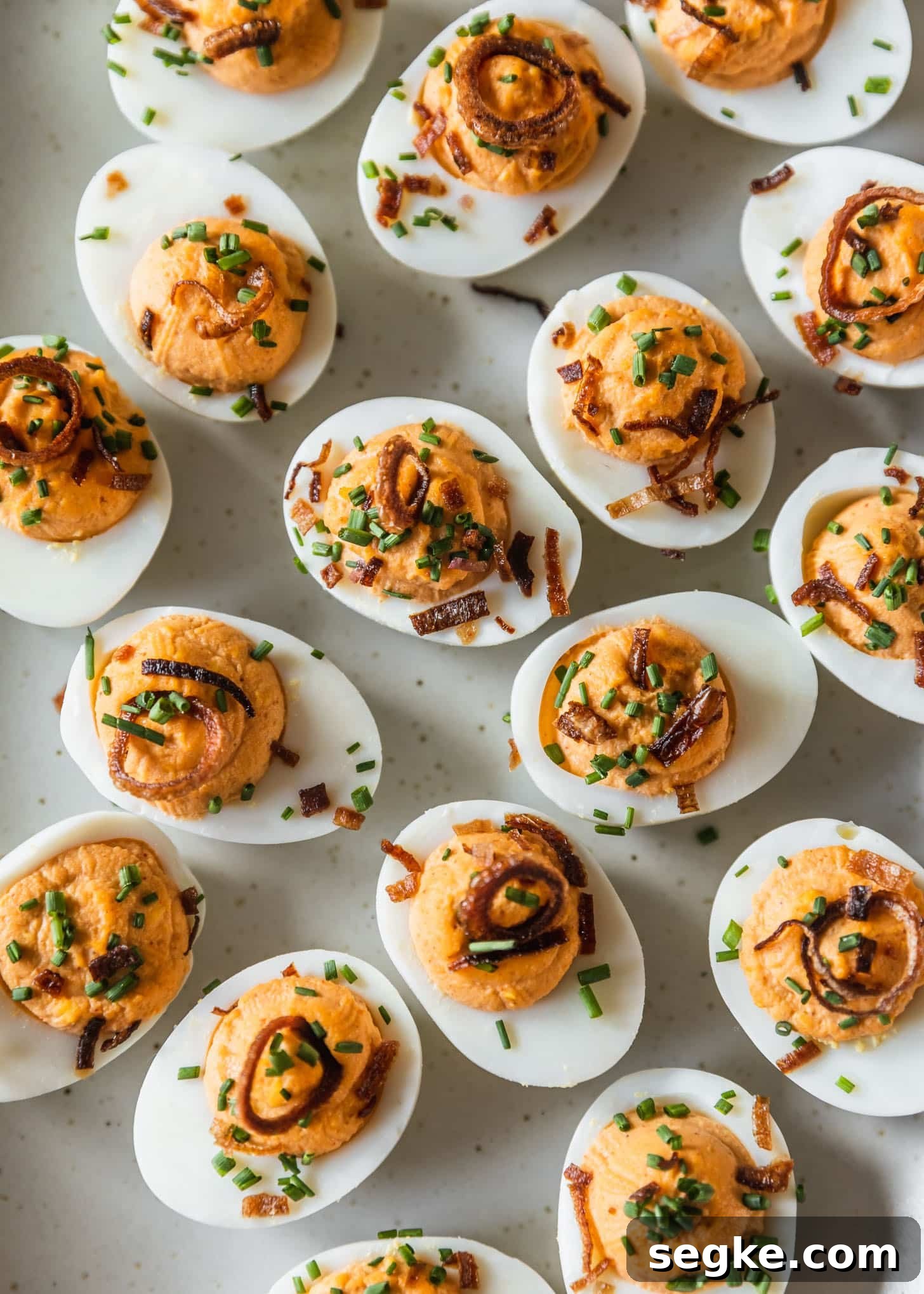 Rows of spicy deviled eggs with crispy shallots and chives on a white tray.