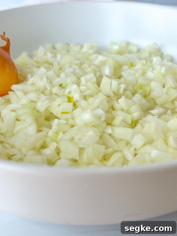 A white bowl filled with finely chopped onions and a whole unpeeled onion resting on the side—perfect for learning kitchen basics like how to shred lettuce.