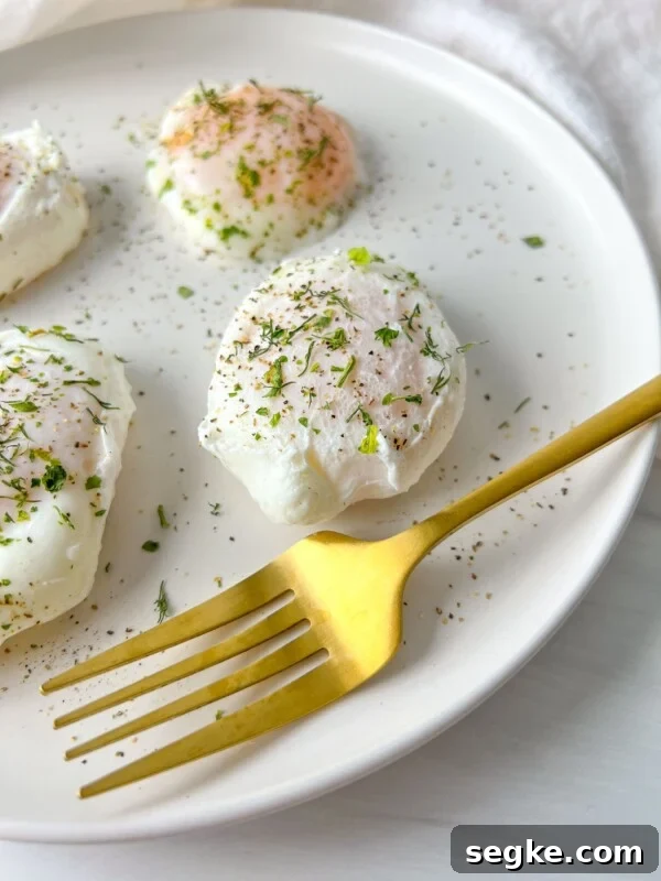 A white plate with three poached eggs sprinkled with herbs and black pepper sits next to a gold fork. The bright, minimal background highlights this perfect example of how to poach eggs beautifully.
