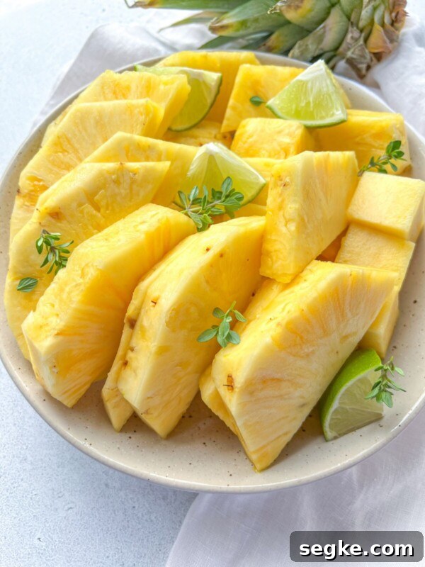 A plate of fresh, sliced pineapple—showcasing how to cut pineapple—arranged with lime wedges and garnished with small green herbs on a light-colored surface.