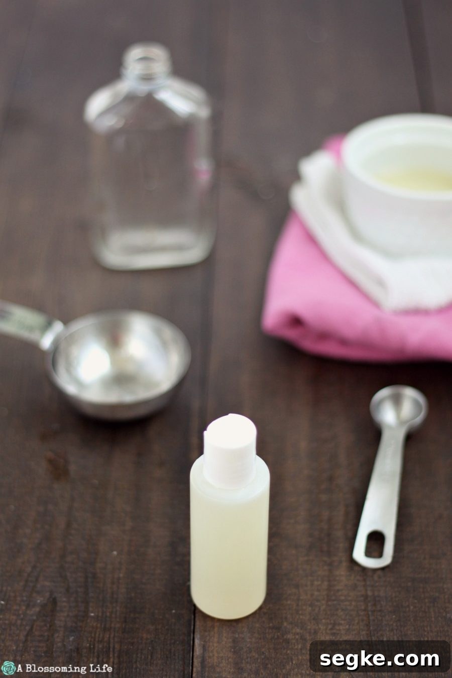 How to Make Natural Hand Sanitizer at Home 2 DIY hand sanitizer in a plastic container on a wood table with measuring cups around