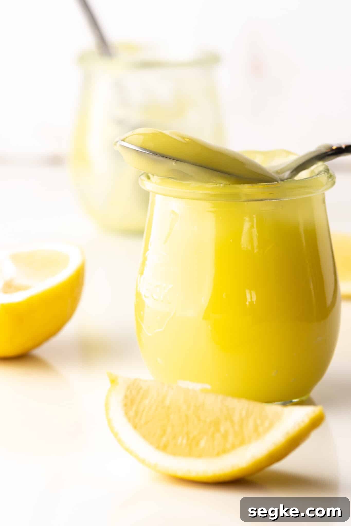Quick Keto Lemon Curd Recipe: Zesty Low-Carb Spread 5 Bright yellow keto lemon curd in a small jar surrounded by pieces of sliced lemons. An empty jar with a spoon is in the background.