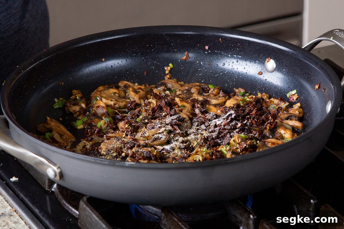 One-Pan Tuscan White Bean Skillet Recipe 9 adding sun-dried tomato and spices to the pan of cooked mushrooms