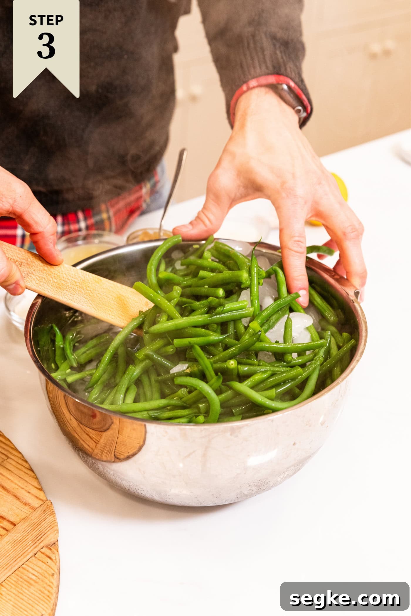 Creamy Homemade Green Bean Casserole Recipe 9 Green beans being placed in ice water bath in a stainless steel bowl to blanch.