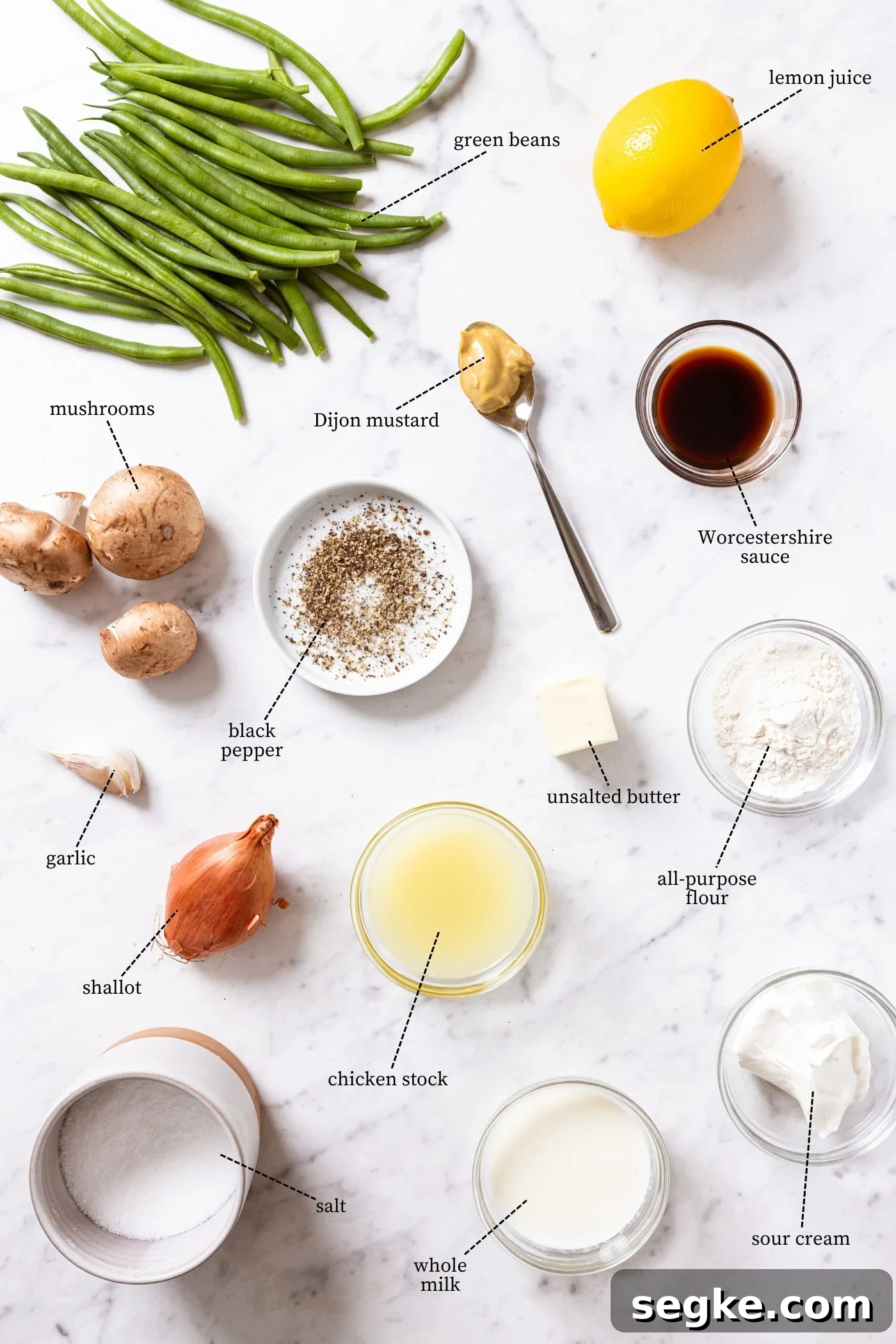 Creamy Homemade Green Bean Casserole Recipe 4 White marble surface filled with all ingredients needed to make green bean casserole including green beans, mushrooms, lemon, shallot, garlic, chicken stock, spices, and more.