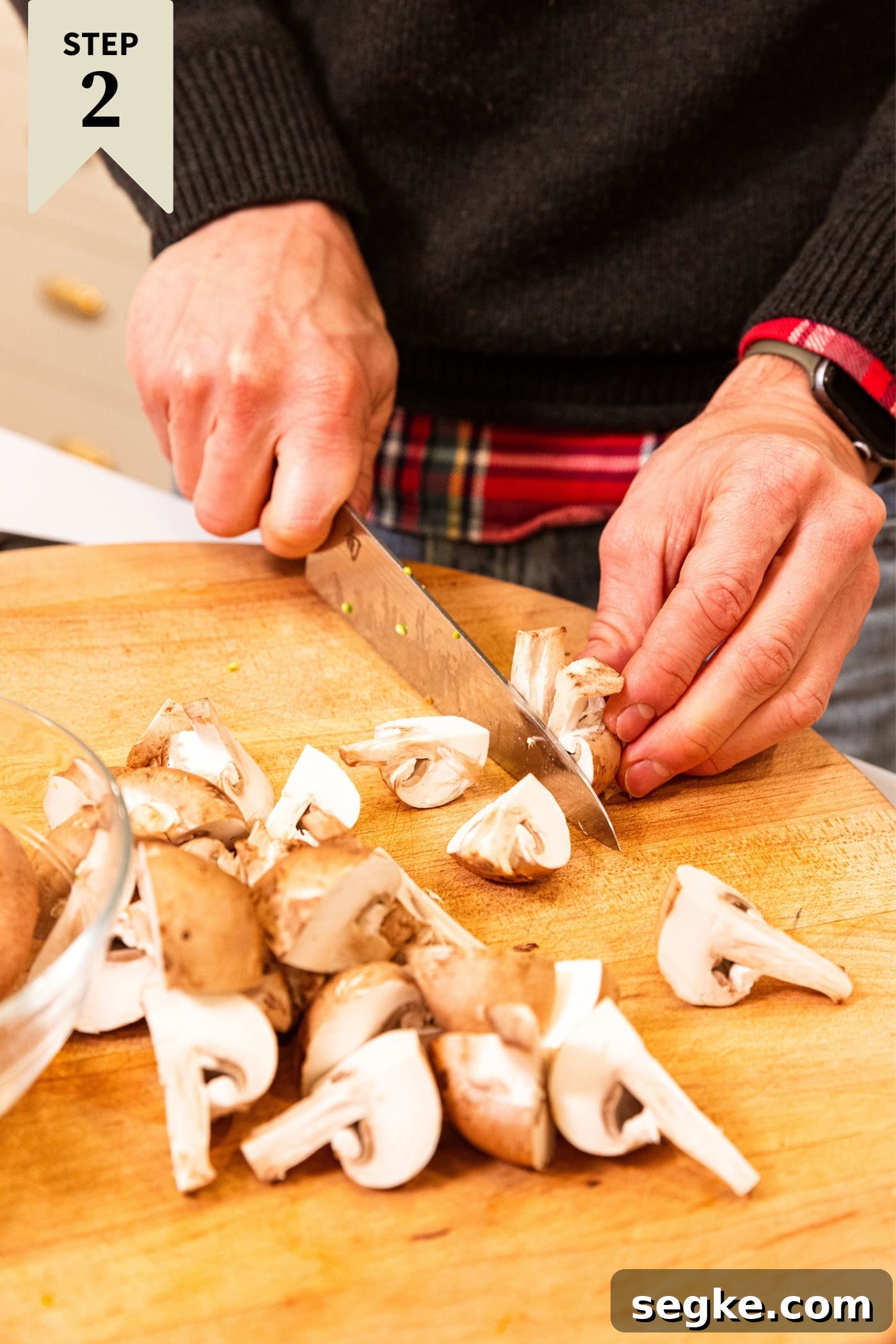 Creamy Homemade Green Bean Casserole Recipe 7 Hand using a knife to slice mushrooms into pieces on a wooden cutting board.