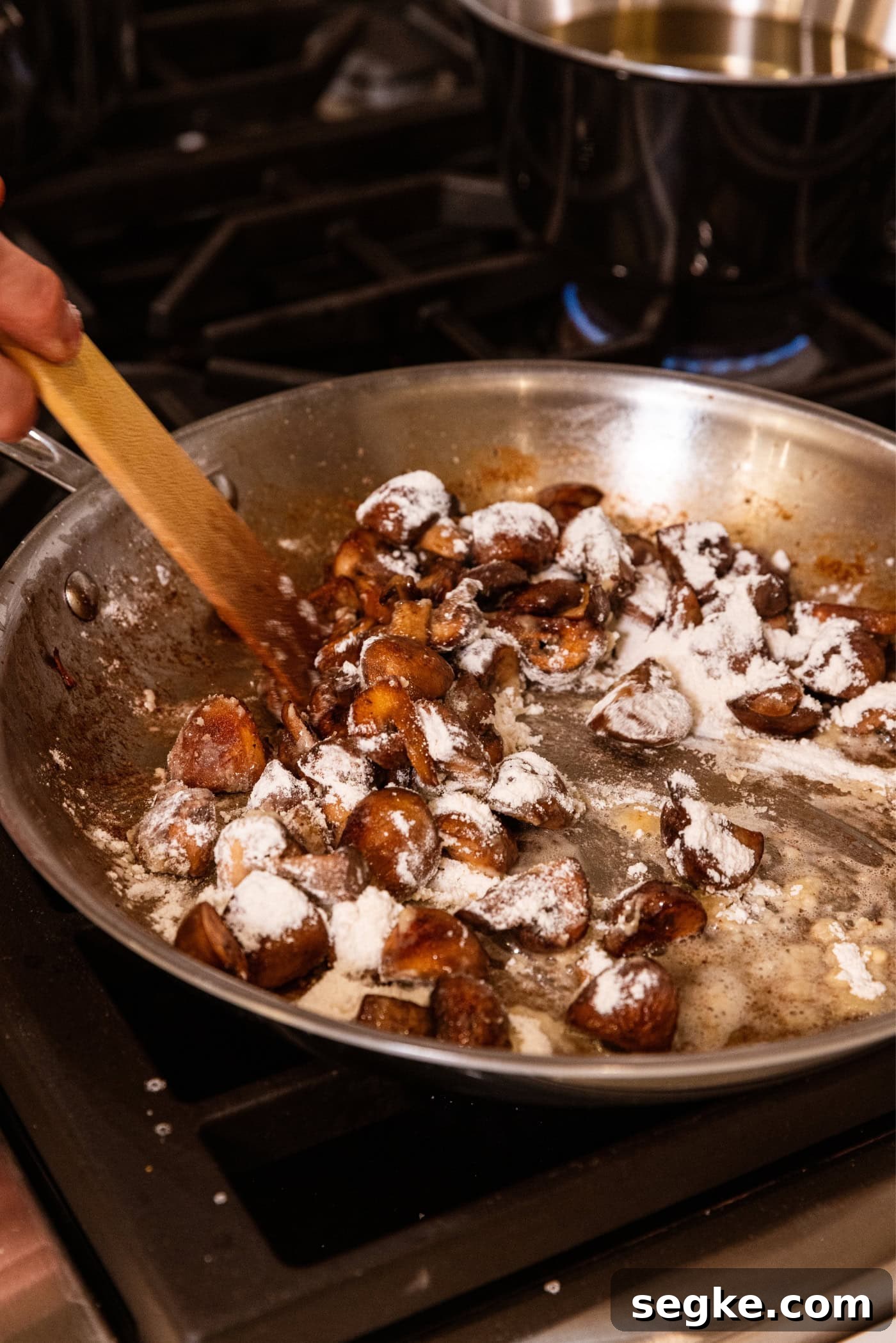Creamy Homemade Green Bean Casserole Recipe 8 Cooking mushrooms being stirred with flour in a stainless steel pan on the stovetop.