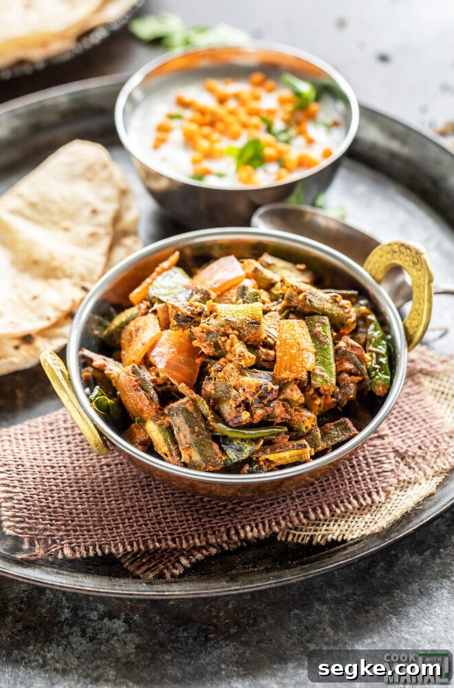 bhindi served in a copper kadai with rotis and a bowl of boondi raita placed in the background