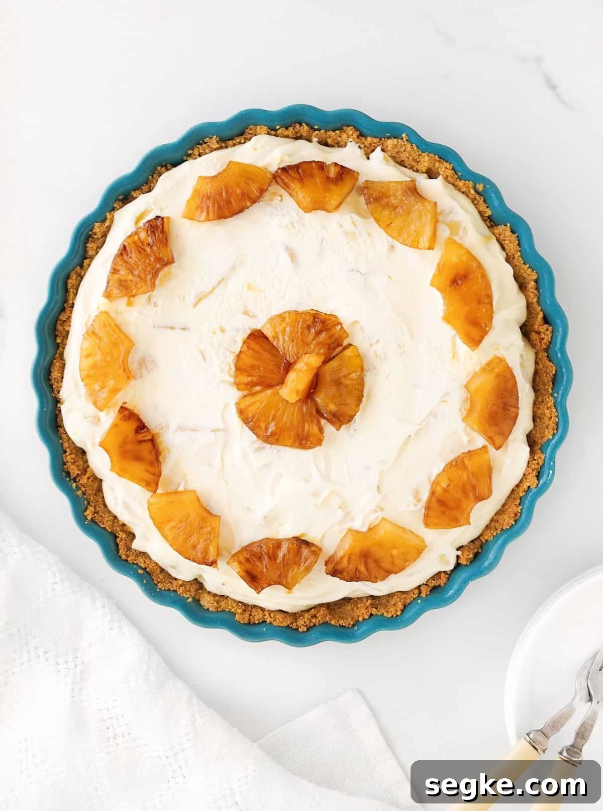 No-Bake Pineapple Cream Cheese Pie 2 Top view of whole pineapple cream cheese pie in a teal dish. White surface.