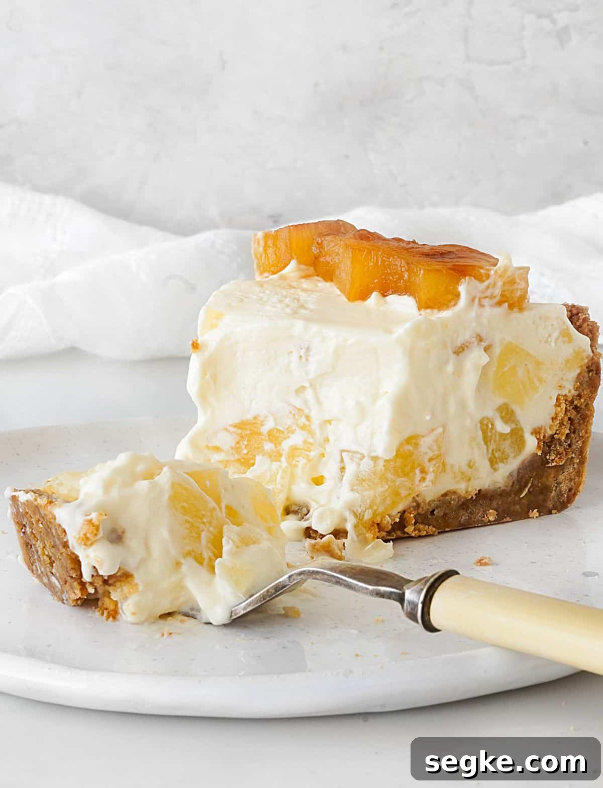 No-Bake Pineapple Cream Cheese Pie 11 Fork on a white plate with bite of pineapple cream pie and eaten slice. Light grey white background.