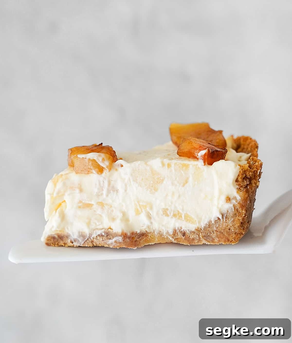 No-Bake Pineapple Cream Cheese Pie 3 Slice of pineapple cream cheese pie on a white cake server. Light grey background.