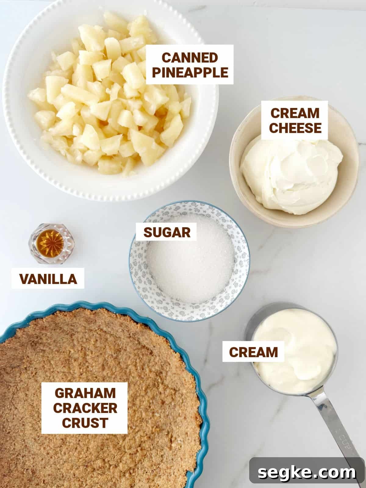 No-Bake Pineapple Cream Cheese Pie 4 Pineapple cream cheese pie ingredients on a white surface including graham crust, sugar, vanilla, cream.