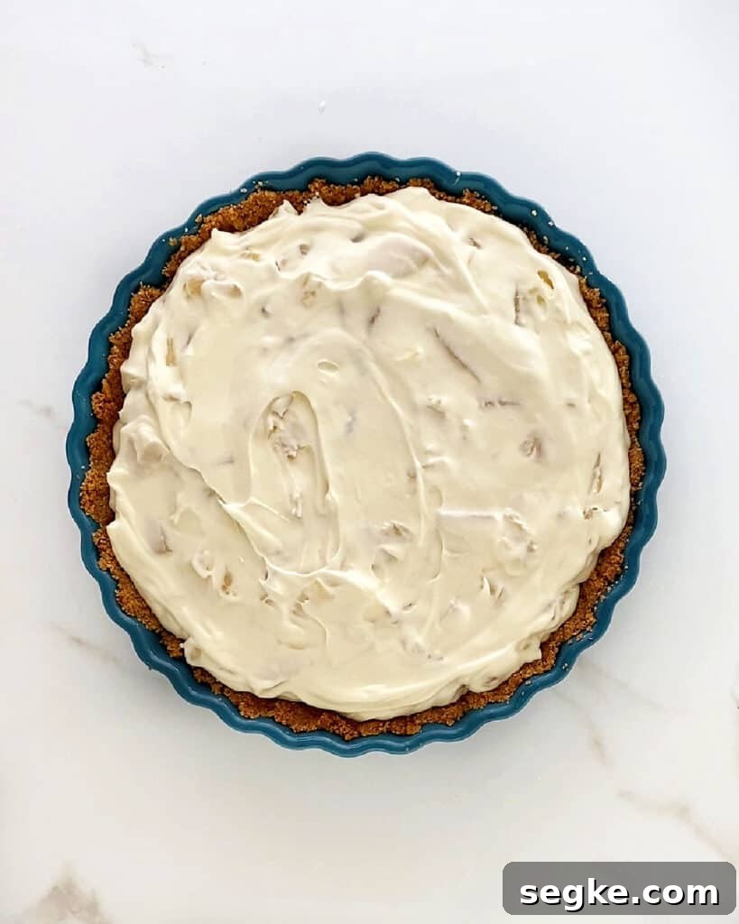 No-Bake Pineapple Cream Cheese Pie 8 Filled crumb crust with pineapple cream cheese mixture. White marbled surface.