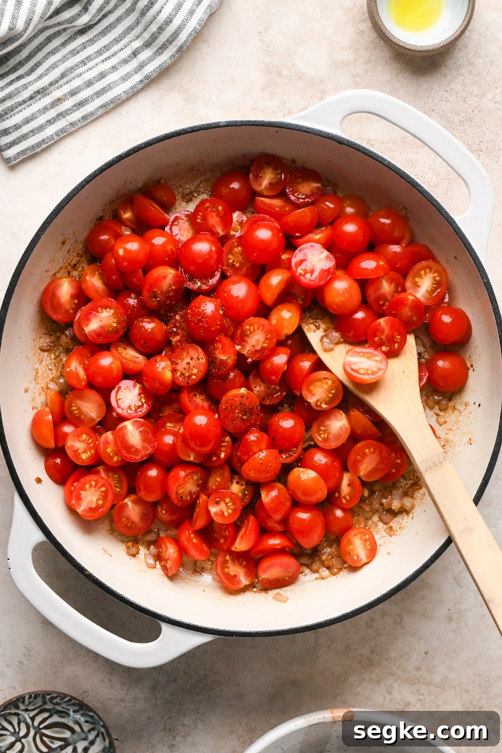 A white skillet filled with halved cherry tomatoes sprinkled with chili flakes.