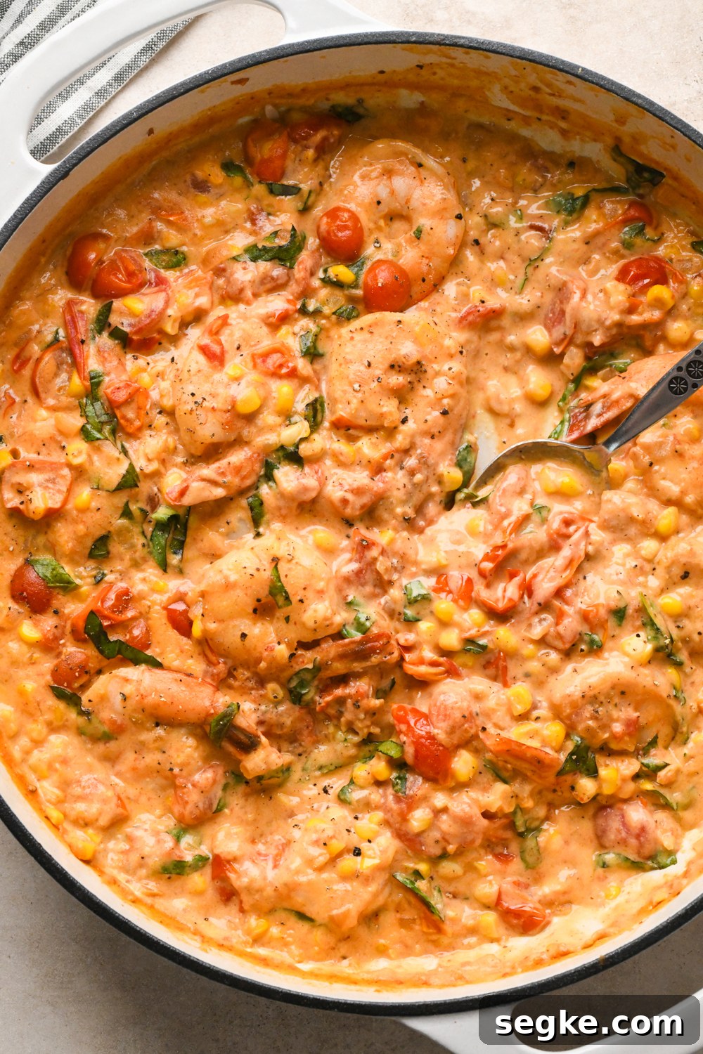 Creamy skillet dish with shrimp, cherry tomatoes, and corn, mixed in a rich, orange-colored cashew cream sauce. A spoon is partially dipped in, ready to serve.