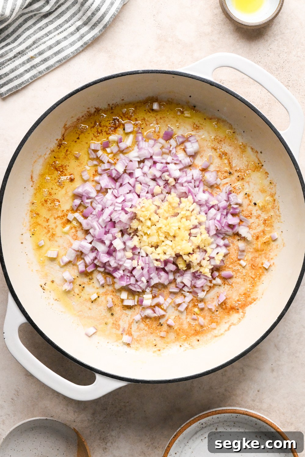 Chopped shallots and minced garlic in a white skillet with a light brown, caramelized base from cooking the shrimp.