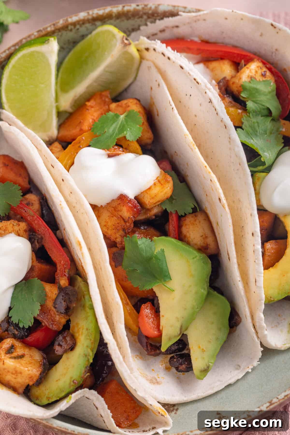 Sheet Pan Halloumi Tacos with Roasted Vegetables 9 A plate of 3 tacos filled with spicy halloumi and black beans, with avocado and soured cream.